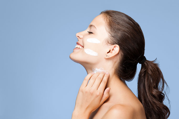 Young woman applying skin cream to face and neck